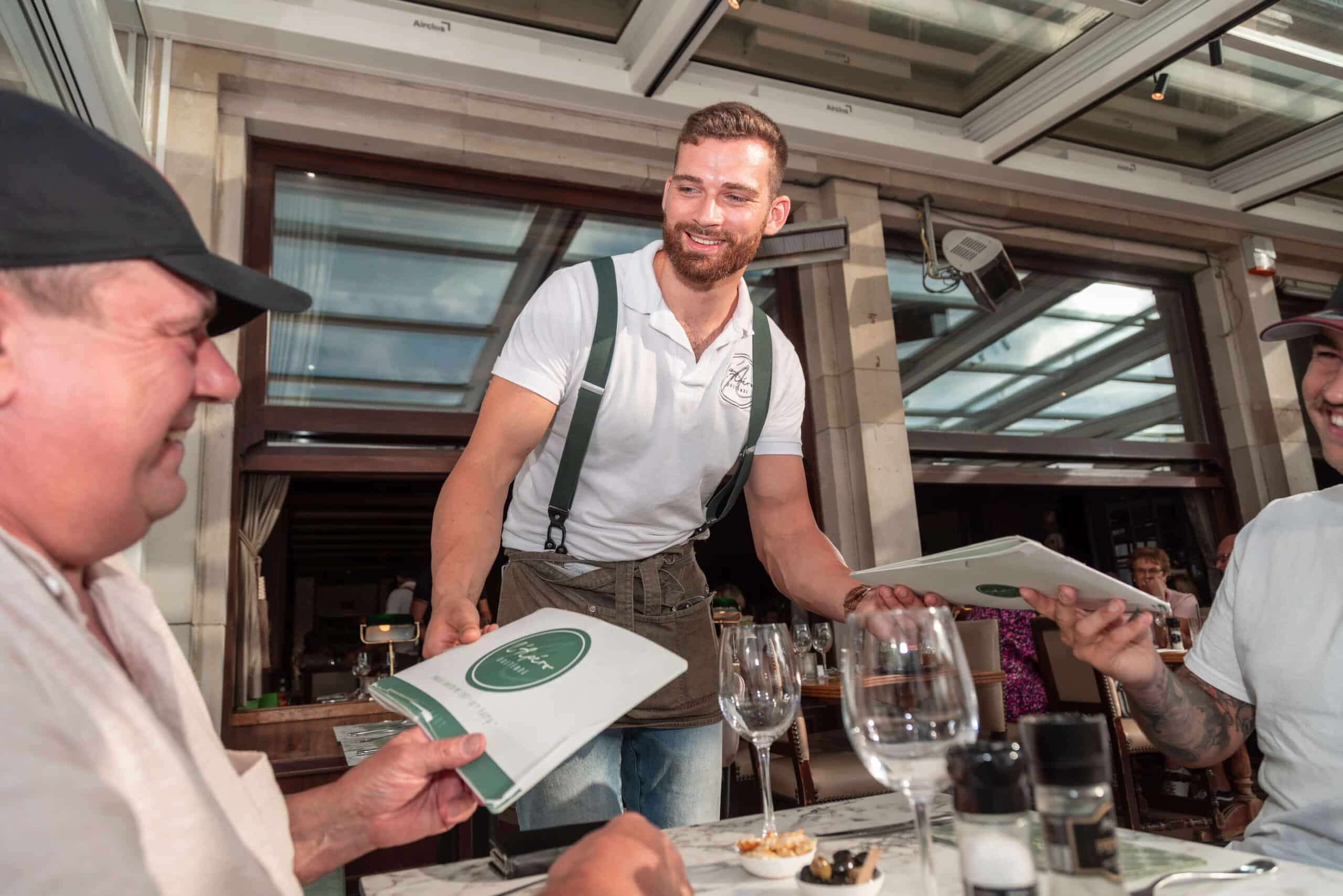 l'Apéro - ober die eetkaarten uitdeelt aan klanten op het overdekt terras